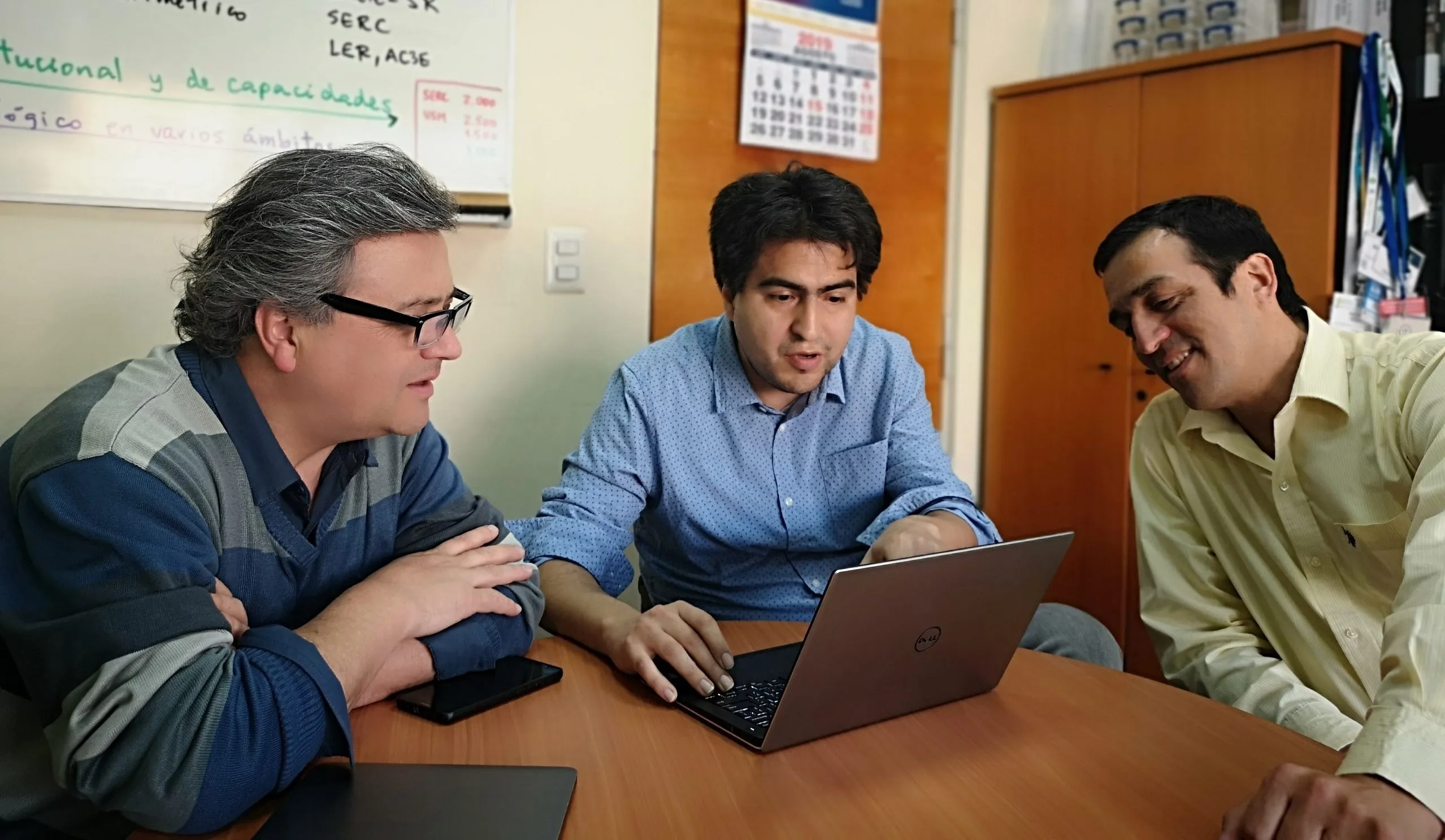 Tres investigadores conversando alrededor de un computador portátil durante una reunión de trabajo.